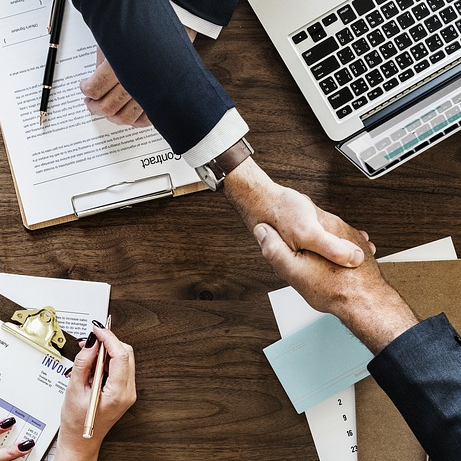 Two people shake hands at Austria Business Center, Dubai, surrounded by documents and a laptop, symbolizing a successful deal.